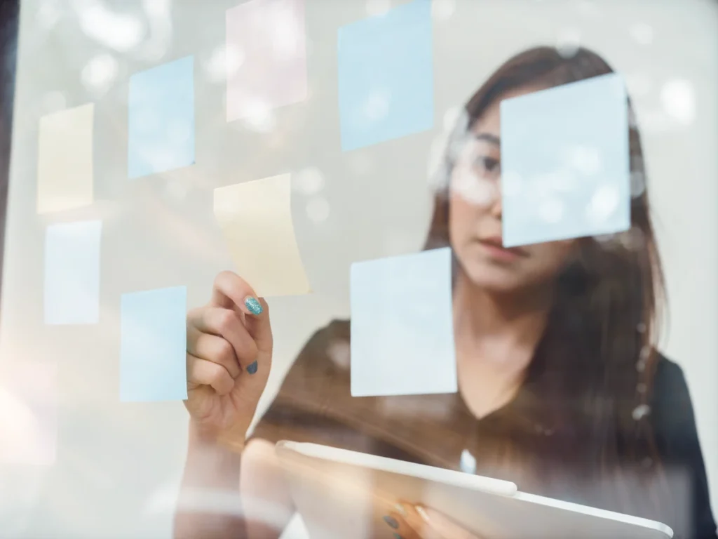 Woman picking up post-it note from glass wall during brand building strategy session in modern office.